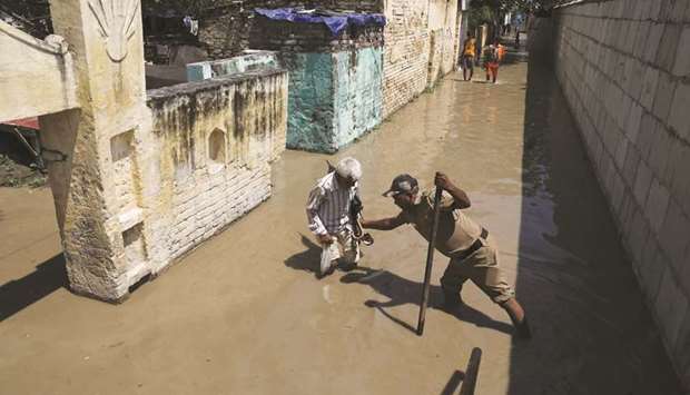 A policeman helps a man to cross a flooded lane on the banks of the river Yamuna in Delhi yesterday.