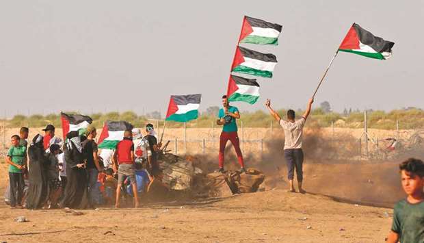 Palestinian demonstrators wave the national flag during clashes between protesters and Israeli forces across the barbed-wire fence following a border demonstration east of Khan Yunis in the southern Gaza Strip, yesterday.