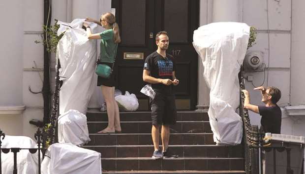 Residents cover up plants at the entrance to residential homes, ahead of Notting Hill Carnival in London, while another resident