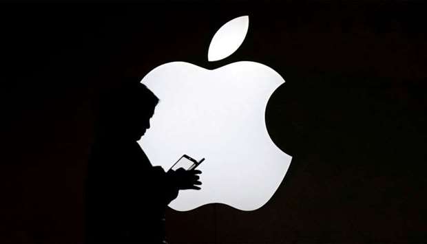 A woman looks at the screen of her mobile phone in front of an Apple logo