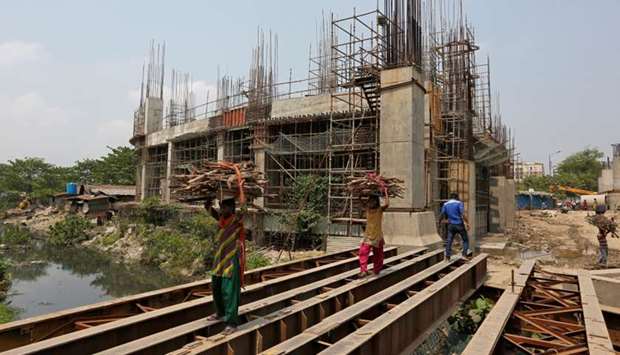 Women carry firewood on iron beams laid over a canal next to the construction site of a metro rail station in Kolkata