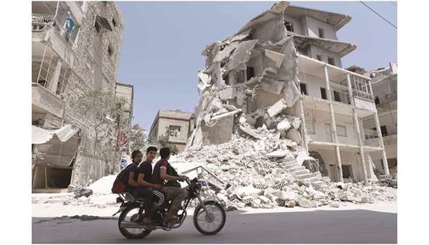 A Syrian man drives a motorcycle past destroyed buildings in the town of Ariha, in the south of Syriau2019s Idlib province, yesterday.