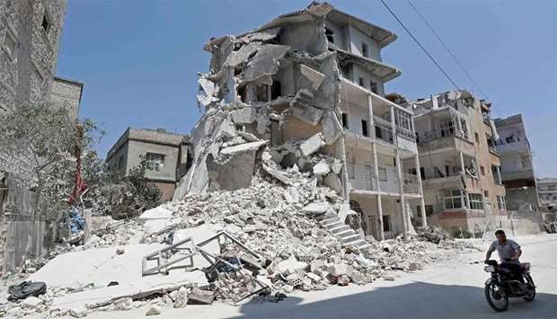 A Syrian man drives a motorcycle past destroyed buildings in the town of Ariha, in the south of Syria's Idlib province
