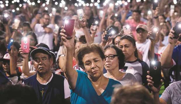 People hold up their phones during a prayer and candle vigil in El Paso, Texas.