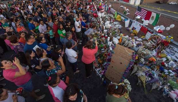 People pray and pay their respects at the makeshift memorial for victims of the shooting that left a total of 22 people dead at the Cielo Vista Mall WalMart (background) in El Paso, Texas