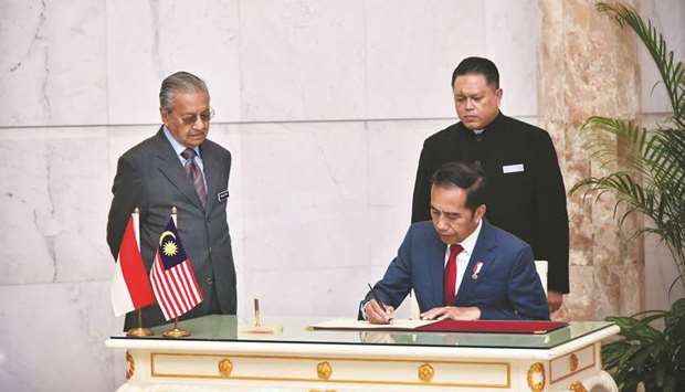 Malaysiau2019s Prime Minister Mahathir Mohamad (left) looks on as Indonesiau2019s President Joko Widodo signs a document during an official welcoming ceremony in Putrajaya. The state oil companies of Malaysia and Indonesia could co-operate or even merge to expand their businesses together, Widodo said yesterday.