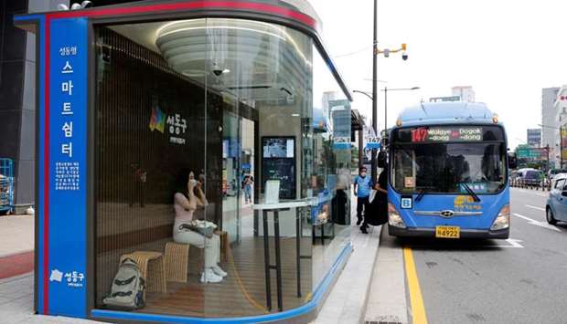 A woman wears a mask inside a glass-covered bus stop in which a thermal imaging camera, UV sterilizer, air conditioner, CCTV and digital signage are set, to avoid the spread of Covid-19 in Seoul, South Korea