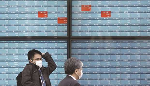 Pedestrians wearing protective masks walk past an electronic stock board outside a securities firm in Tokyo. Stocks in Asia Pacific have dug their way out of a hole for the year as the global market recovery from the coronavirus continues to grind higher. A record high set in early 2018 seems to be the next target for investors.