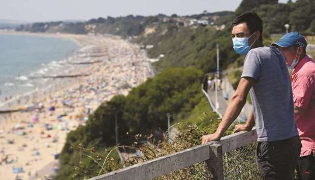 Men wearing protective face masks observe the crowded Bournemouth Beach.