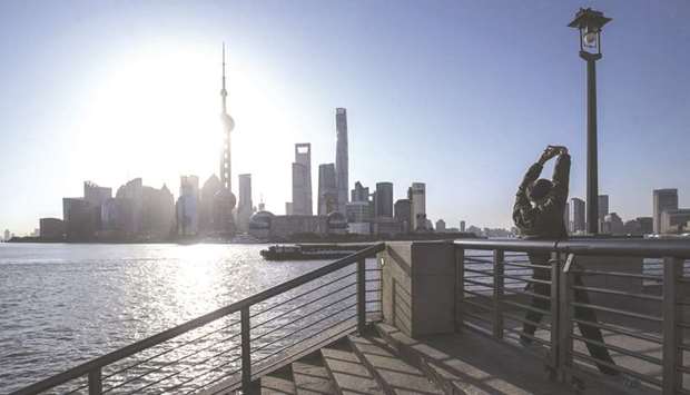 A man stretches on the Bund as skyscrapers of the Pudong Lujiazui Financial District stand across the Huangpu River during sunrise in Shanghai.