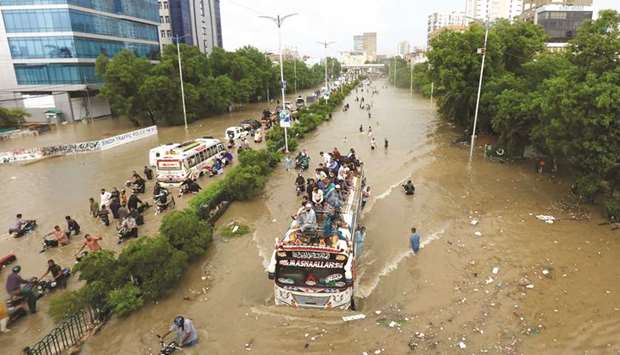 People sit atop a bus roof while others wade through the flooded road in Karachi.