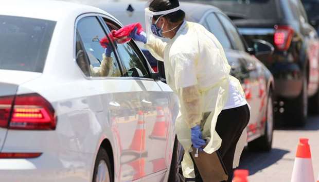 A worker passes testing bags to a passenger at a drive-in Covid-19 testing center at Charles R. Drew University of Medicine and Science in South Los Angeles on July 31