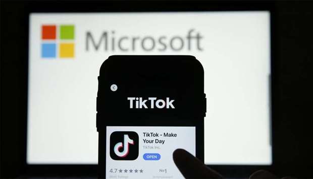 A smartphone screen displays the app store view of TikTok in front of a Microsoft logo displayed on a laptop screen in London.