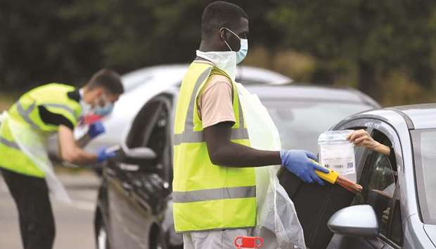 Officials deliver and collect testing kits through car windows at a mobile drive through coronavirus disease testing centre, in Richmond, London, yesterday.