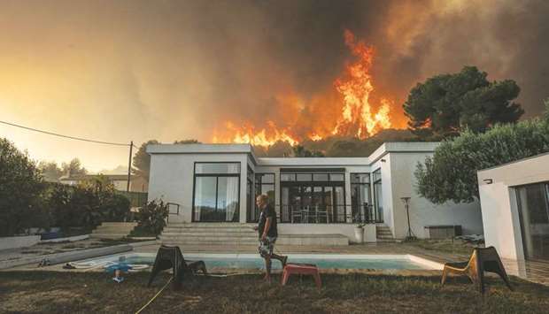 A man walks with a garden hose to drench his house in La Couronne, near Marseille, before being evacuated as a wildfire burns in the background.