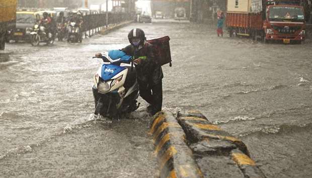 A delivery boy pushes his scooter after it stopped working along a waterlogged road following heavy rainfall in Mumbai yesterday.