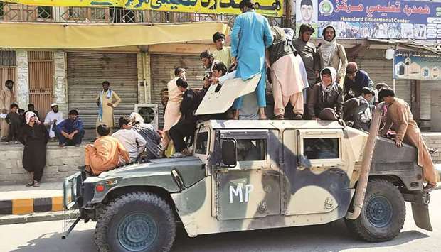 BACK IN BUSINESS: Taliban fighters and local residents sit over an Afghan National Army humvee vehicle along the roadside in Laghman province. (AFP)
