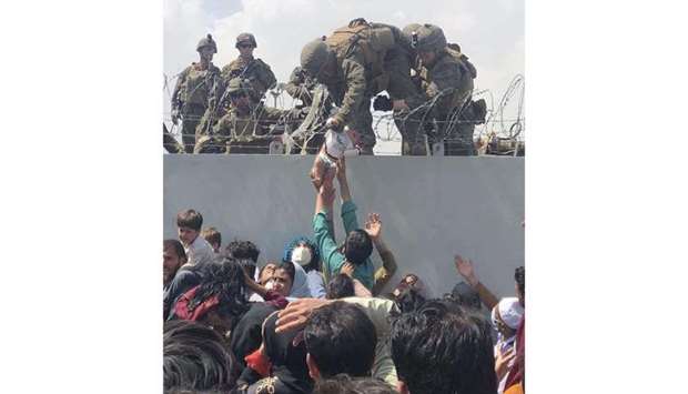 This image made available to AFP by Omar Haidiri, shows a US Marine grabbing an infant over a fence of barbed wire during an evacuation at Hamid Karzai International Airport in Kabul on August 19, 2021. 