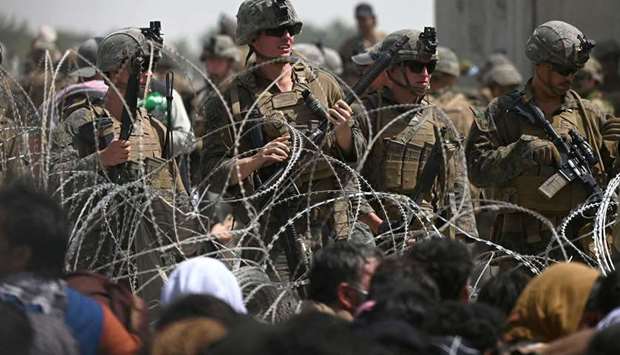 US soldiers stand guard behind barbed wire as Afghans sit on a roadside near the military part of the airport in Kabul, hoping to flee from the country.