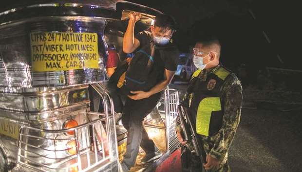 A policeman inspects a vehicle with passengers at a checkpoint placed to prevent the spread of Covid-19, in Quezon City, Metro Manila, Philippines, yesterday.