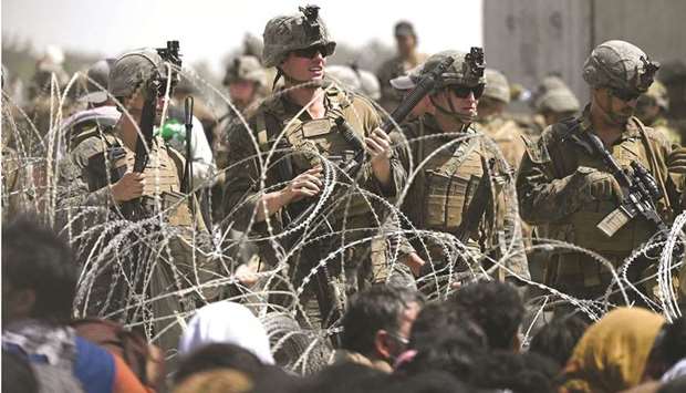 AFTERMATH: US soldiers stand guard behind barbed wire as Afghans sit on a roadside near the military part of the airport in Kabul last Friday, hoping to flee from the country after the Talibanu2019s military takeover of Afghanistan. (AFP)
