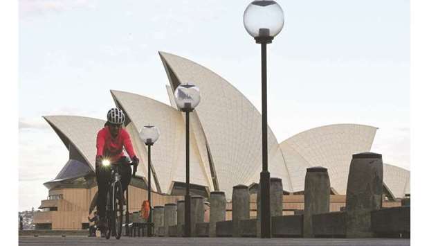 A woman rides on a bicycle in front of the landmark Sydney Opera House during lockdown yesterday.
