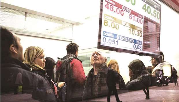 A sign displaying US dollar, euro, Brazilian real, and Chilean peso exchange rates is displayed as people wait inside a currency exchange house in Buenos Aires. Some of the yearu2019s best-performing emerging-market currencies may lose favour as the rationale for rate hikes to tackle inflation shows early signs of waning.