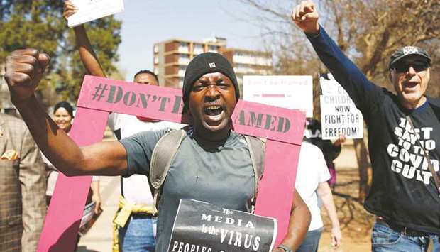 Demonstrators raise their fists and react to a slogan while holding up banners and placards during a protest march against Covid-19 vaccinations and wearing of masks, in Pretoria.