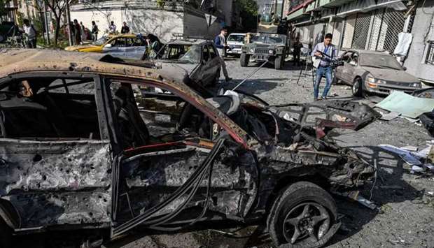 Journalists and security personnel are seen in the backdrop of the wreckage of a car a day after an explosion in Kabul Wednesday. AFP