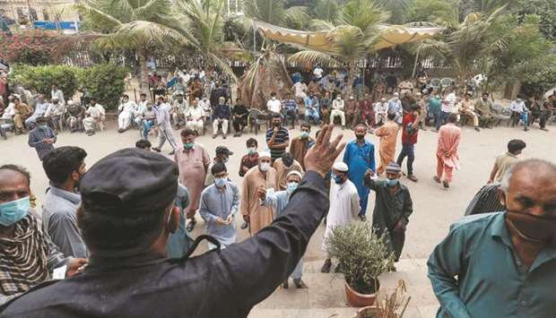 An officer calls out to residents with their registration numbers, who are waiting to receive a dose of coronavirus vaccine, outside a vaccination facility in Karachi.