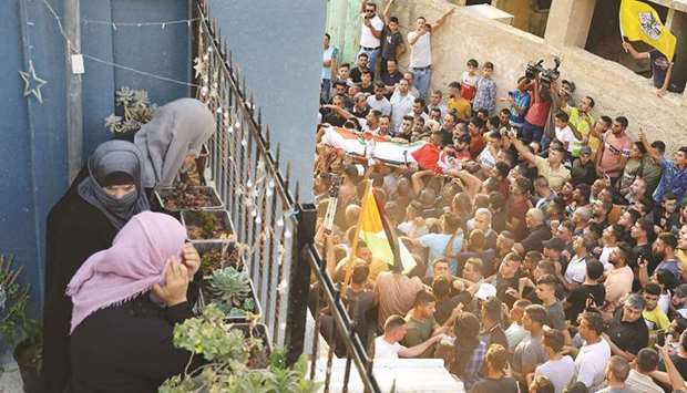 Women watch from a balcony as Palestinians carry the body of the protester during his funeral in the occupied West Bank town of Beita.