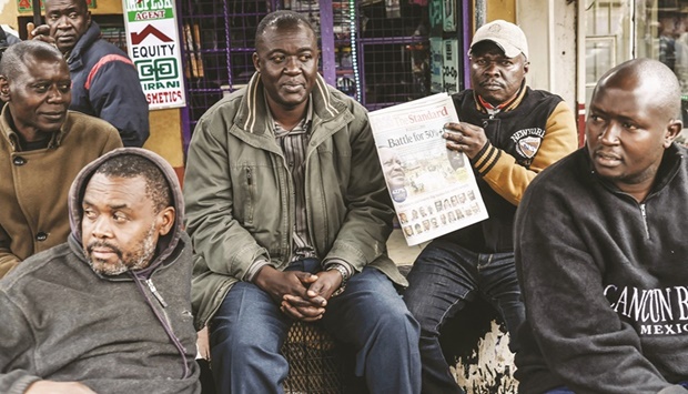 A man holds The Standard, a Kenyan daily newspaper, as he sits with others at a newsstand in Mathare, Nairobi.