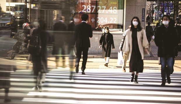 Pedestrians cross a street in front of a stock indicator displaying numbers of Nikkei 225 of the Tokyo Stock Exchange in Tokyo (file). Japanu2019s outlook has been clouded by a resurgence in Covid infections, slowing global growth, supply constraints and rising raw material prices that are boosting householdsu2019 living costs.
