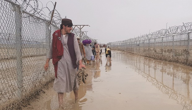 Afghanistan and Pakistan nationals walk along a muddy fenced corridor as they enter Pakistan at a Pakistan-Afghanistan border crossing point in Chaman.