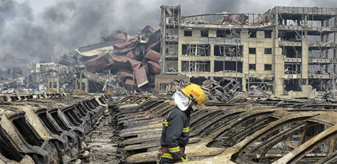 A firefighter walks among damaged vehicles as smoke rises amidst shipping containers at the site of explosions in Tianjin
