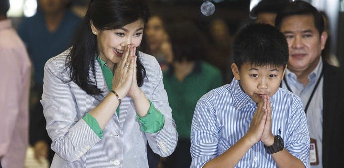 Former Thai Prime Minister Yingluck Shinawatra and her son Supasek Amornchat (right) gesture in a traditional greeting to the media as they arrive at 