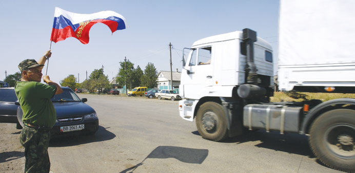 A local resident holds a Russian flag as trucks, part of a Russian humanitarian convoy, crosses the Ukrainian border at the Izvarino custom control ch