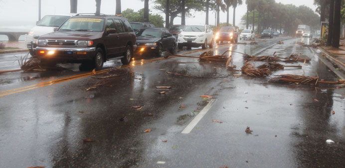 Cars drive in the rain and past fallen pieces of palm trees in Santo Domingo, Dominican Republic.