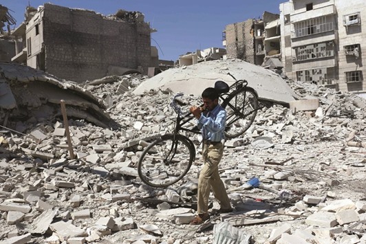 A Syrian man carrying a bicycle makes his way through the rubble of destroyed buildings following a reported air strike on the rebel-held Salihin neighbourhood of the northern city of Aleppo, yesterday. Air strikes have killed dozens in rebel-held parts of Syria as the opposition considers whether to join a US-Russia truce deal due to take effect today.