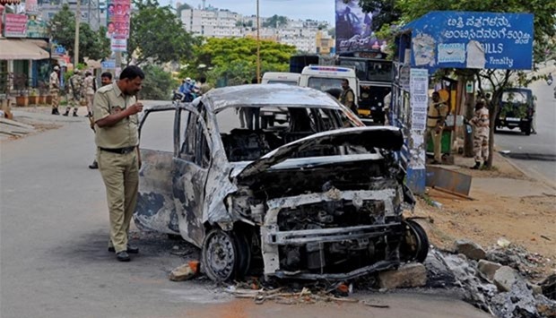 A police officer inspects the charred remains of a car set ablaze in Bengaluru on Tuesday.