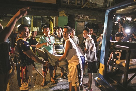 Residents carry the body of a suspected drug dealer killed by unidentified gunmen in Manila yesterday.