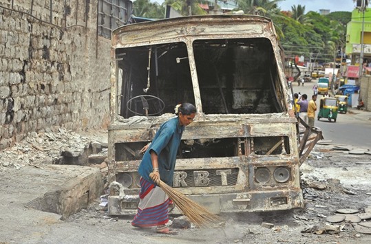 A municipal worker sweeps around the charred remains of a lorry set ablaze during the violent protests in Bengaluru yesterday.