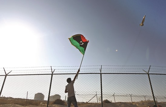 A man waves a Libyan flag as fighter jet flies by at the Zueitina oil terminal on Wednesday. Libyau2019s state oil company on Wednesday lifted curbs on crude sales from the ports of Ras Lanuf, Es Sider and Zueitina, potentially unlocking 300,000 bpd of supply.