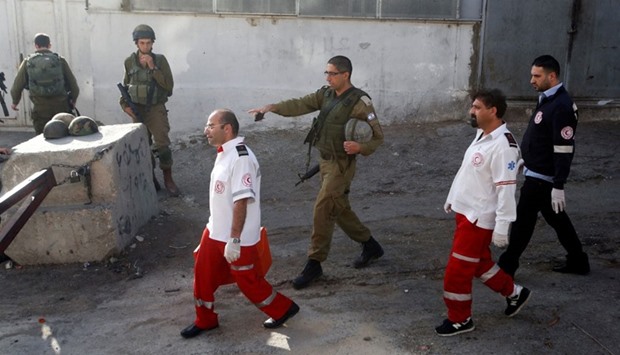 Israeli forces and Palestinian medics walk near the scene of what the Israeli military said was a stabbing attack by a Palestinian, in Tal-Rumida in the West Bank city of Hebron yesterday