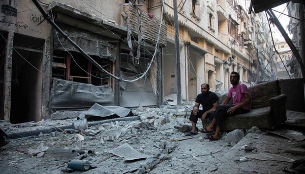 Syrians sit and look at the rubble following an air strike on the rebel-controlled neighbourhood of Karm al-Jabal