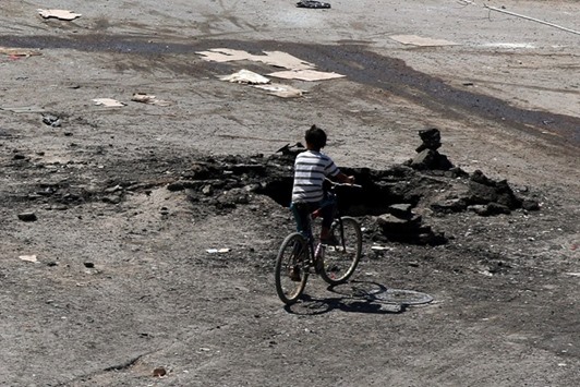 A boy rides a bicycle near a hole in the ground after an airstrike on Sunday in the rebel-held town of Dael, in Deraa Governorate, Syria.