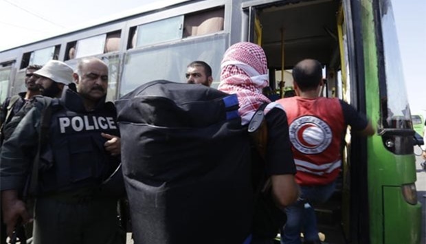 Syrian policemen stand guard as Red Crescent members help opposition fighters and their families carry their belongings into a bus at a Syrian army checkpoint on the edge of the rebel-held Waer neighbourhood in Homs on Thursday.