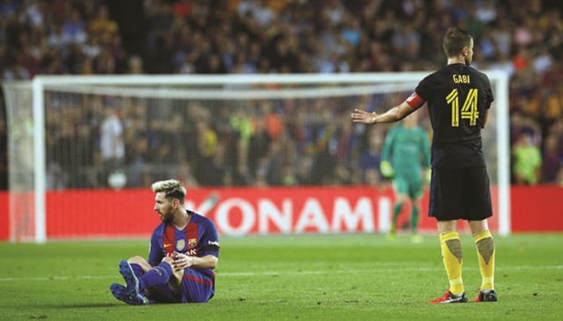 Barcelonau2019s Lionel Messi sits on the turf after a foul on him next to Atletico Madridu2019s Gabi Fernandez.