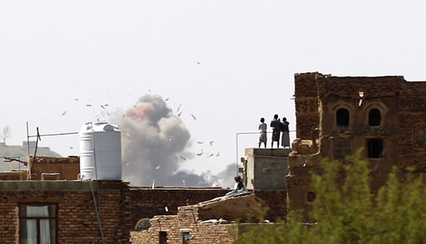 Yemenis stand on a rooftop looking at smoke billowing from a building following a reported air strike carried out by the Saudi-led coalition in the Yemeni capital Sanaa.
