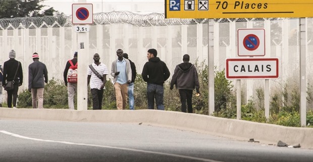 Migrants living in the u2018Jungleu2019 migrant camp walk past a sign posted along a road that leads to Calais.